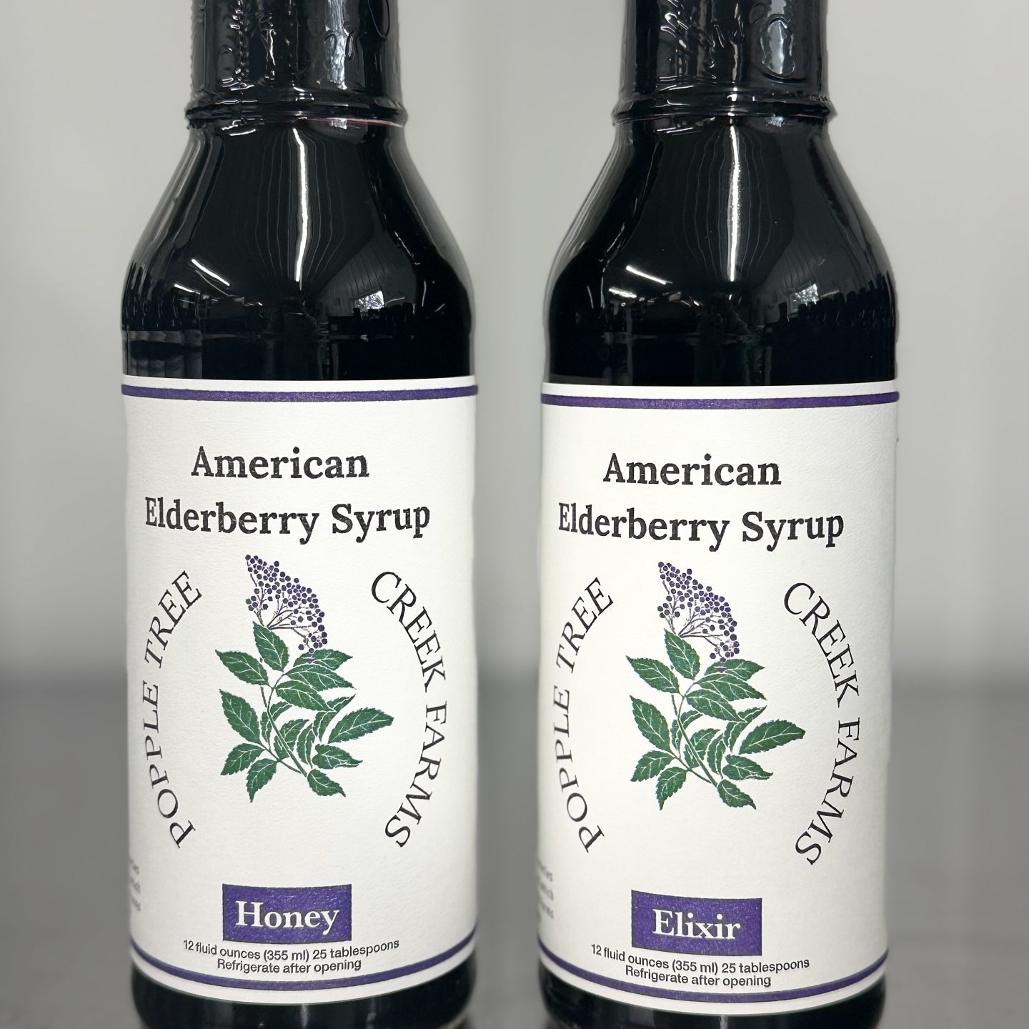 two glass bottles, both read american elderberry syrup, one reads honey the other reads elixir