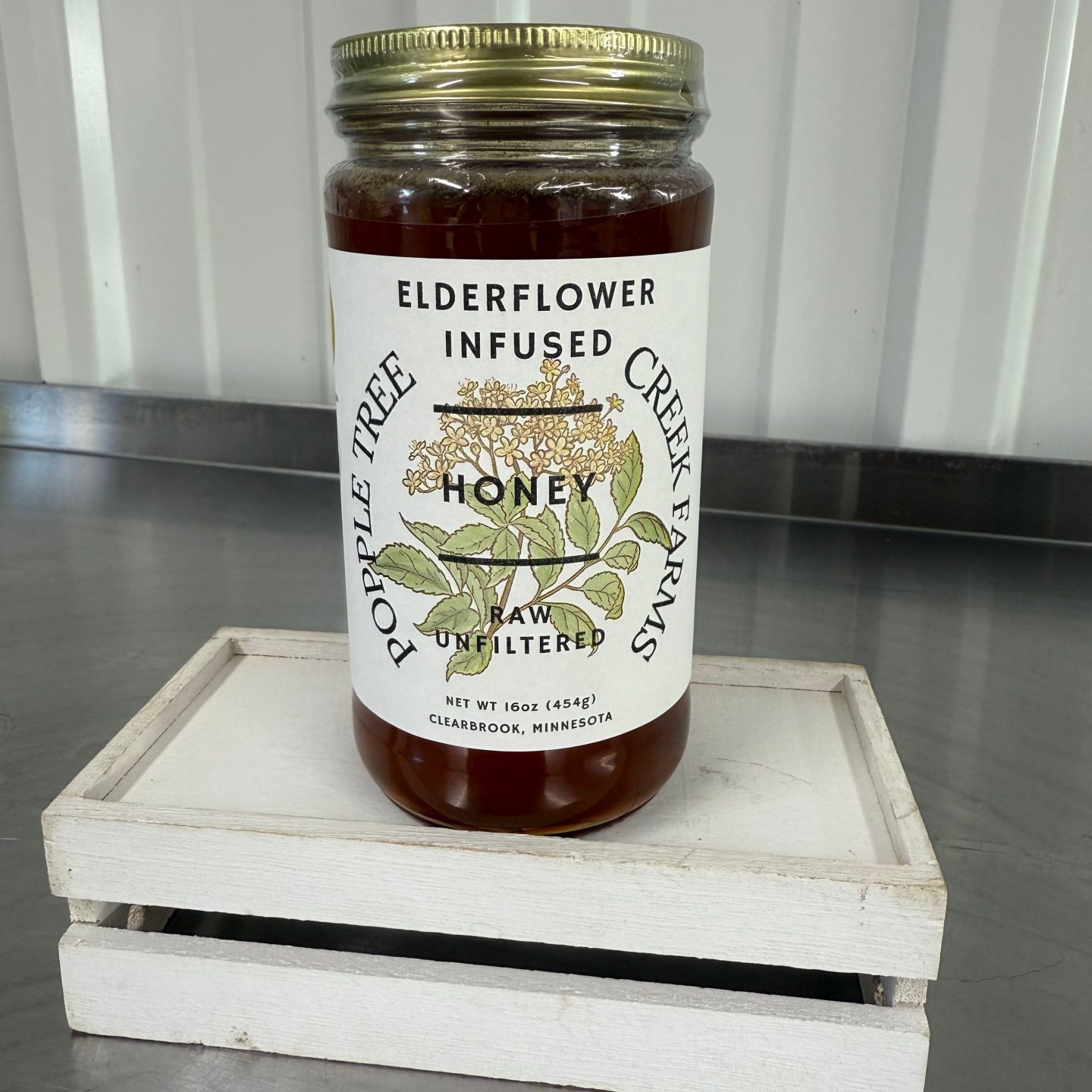 large glass jar of elderflower infused honey on a small white crate