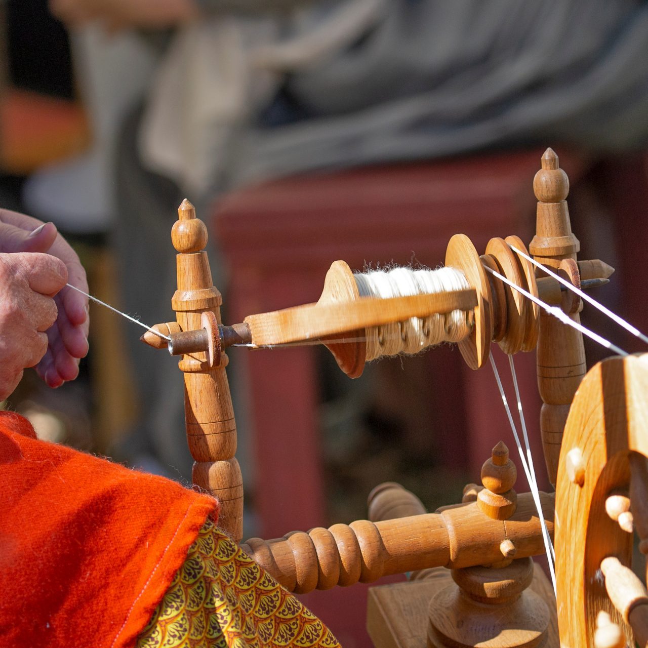 a woman's hands spin white wool yarn on a spinning wheel