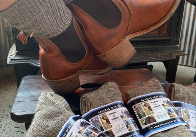 Natural fiber socks displayed in front of a wood stove with booted feet.