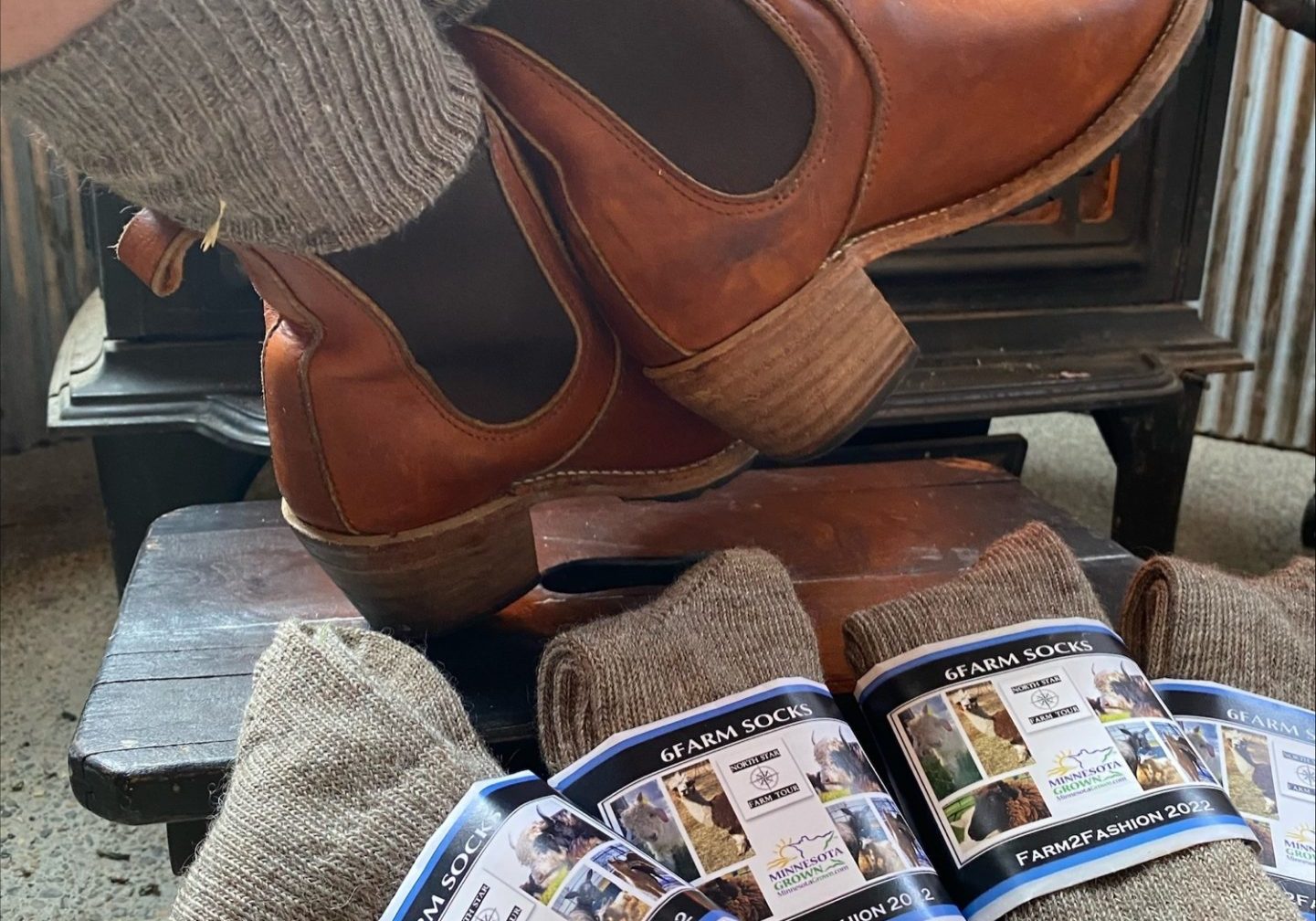 Natural fiber socks displayed in front of a wood stove with booted feet.