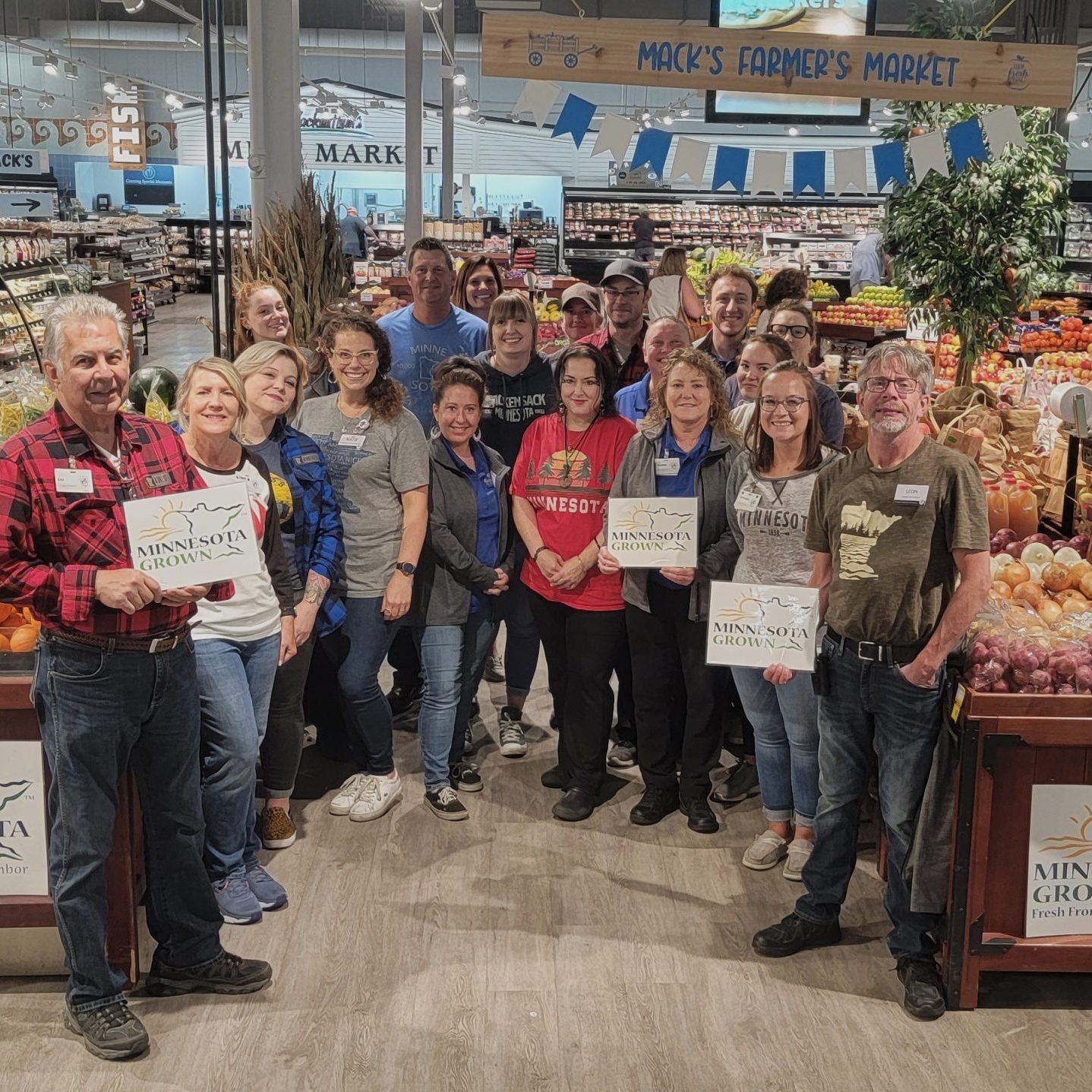 A group of grocery store staff gathered in their produce display. Many of them hold Minnesota Grown signs.