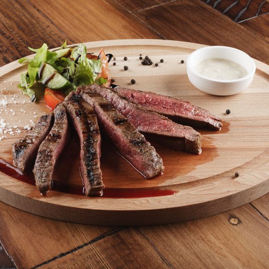 Flank steak with salad and sauce on wooden surface