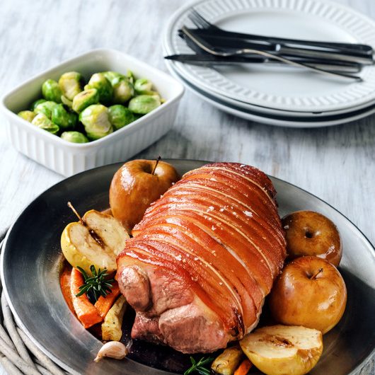 Whole pork shoulder roast with apple and vegetables, served on a table, traditional sunday lunch
