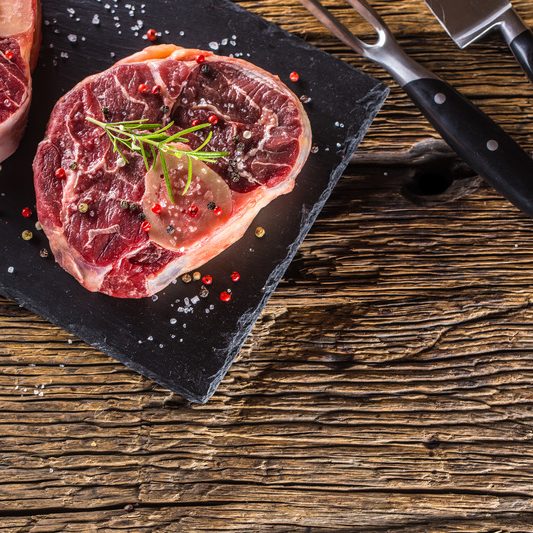 Two pieces raw beef shank on slate board and wooden table.